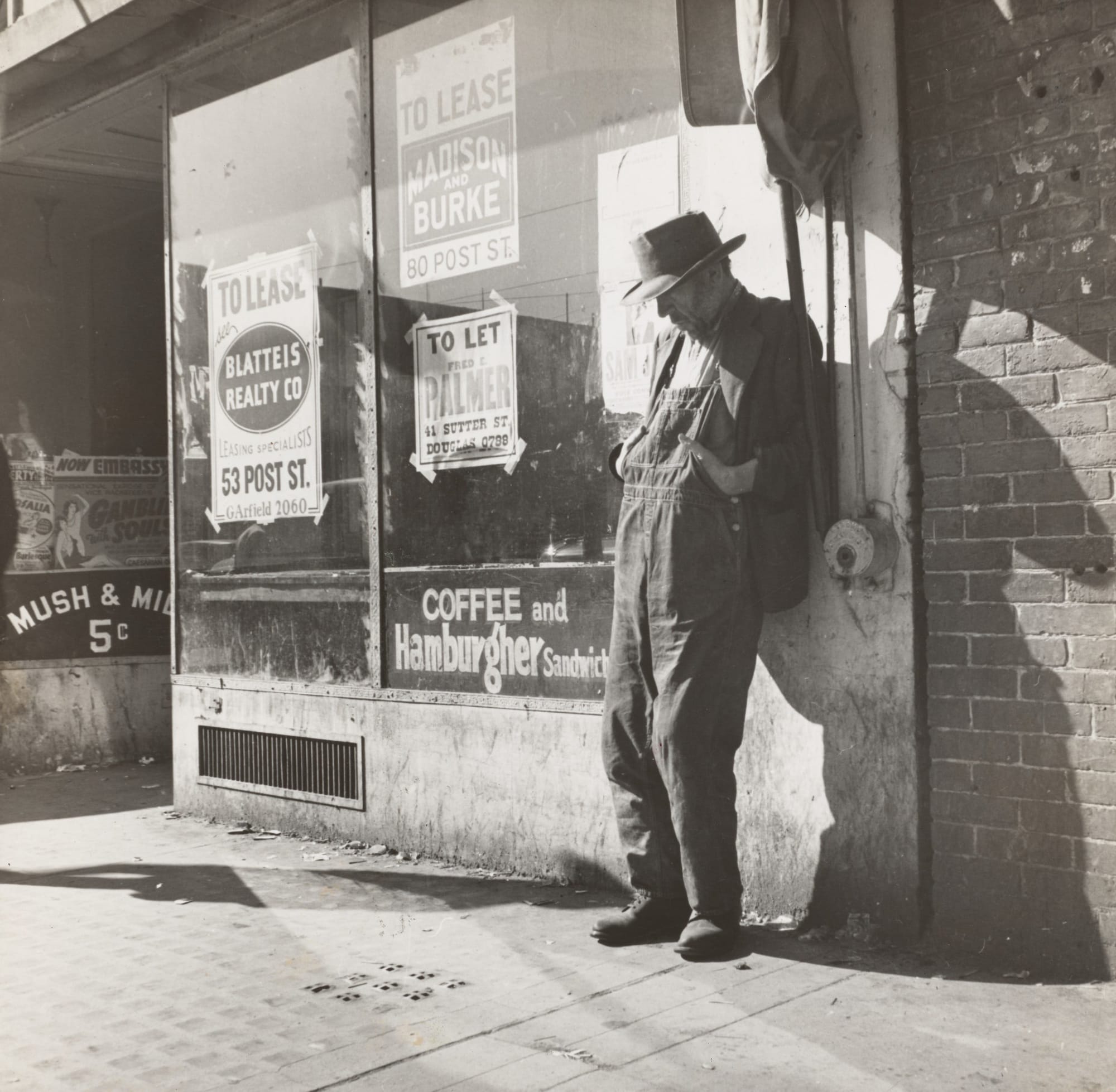 A black and white photo of a man standing beside a wall papered with "to let" signs.