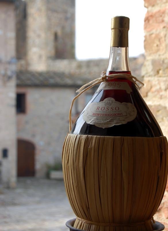 A bottle of red wine with a rounded bottom in a straw basket
