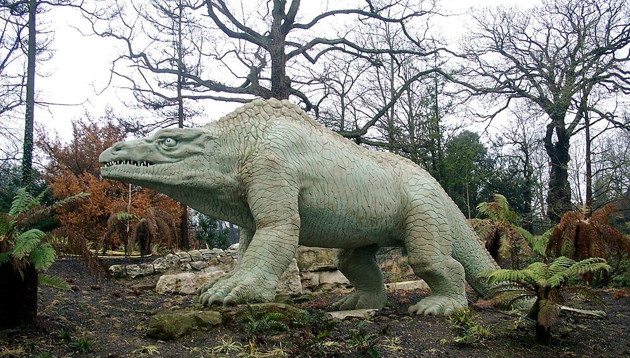 A sculpture of a Megalosaurus in a park in London. The dinosaur is walking on four feet.