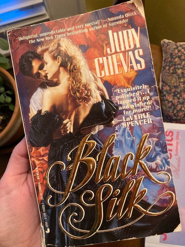 paperback copy of Black Silk by Judy Cuevas, showing a white couple in 1850s clothes undressing and embracing