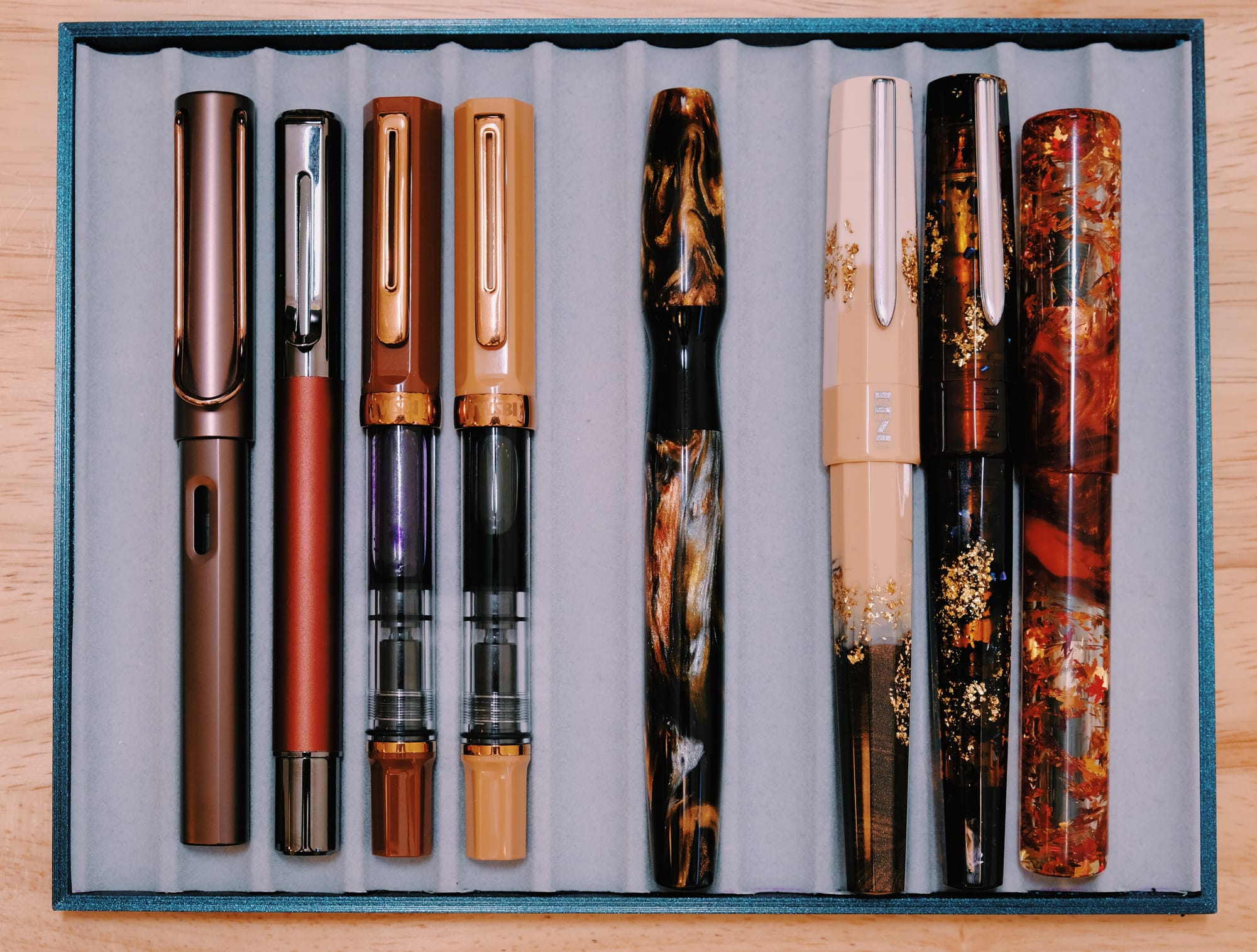 Various brown fountain pens from different brands in a tray on either side of the Noldor (4 on left, 3 on right)