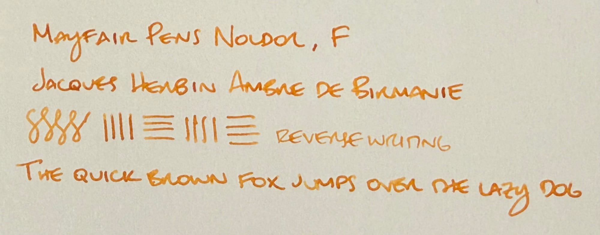 Writing sample written with an amber brown ink: "Mayfair Pens Noldor, F; Jacques Herbin Ambre de Birmanie; [figure-8s, horizontal and vertical lines], 'reverse writing' written with nib upside down; The quick brown fox jumps over the lazy dog"