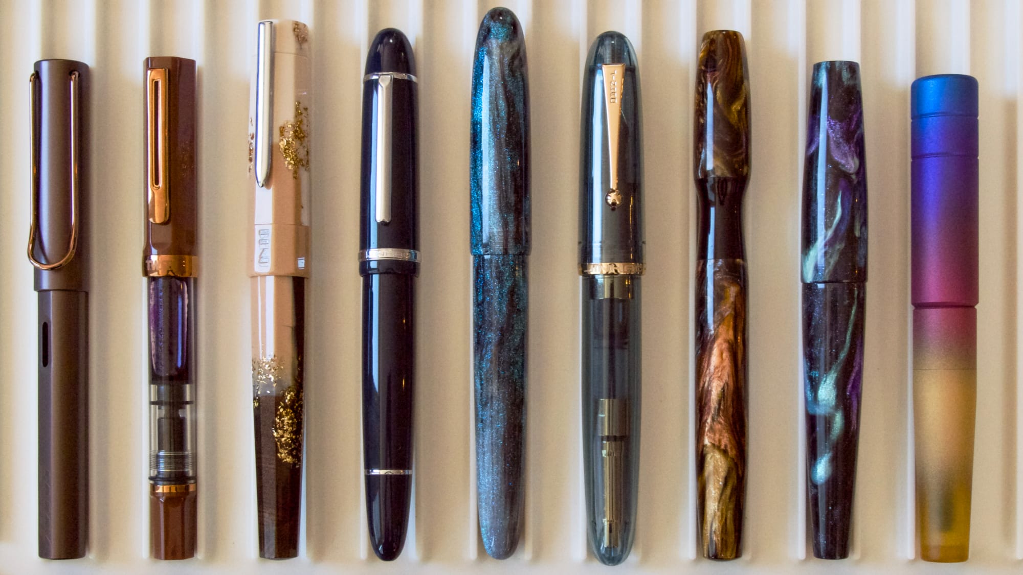 9 fountain pens of varying sizes and designs sitting on a white tray, with the Asvine C80 in the middle