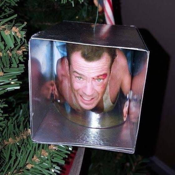 A Christmas tree ornament depicting John McClane crawling through an air duct with a lighter; the box is silver cardboard, and a curved picture of the scene is placed inside to mimic him crawling in the air duct