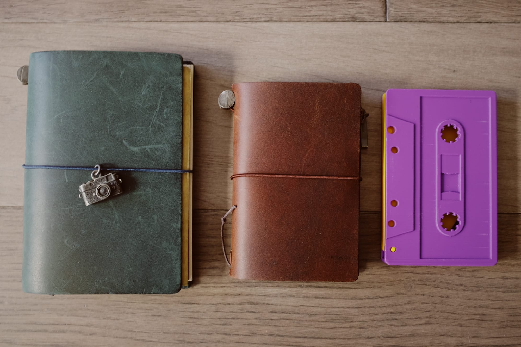 Same as image above, but with a purple and yellow 3D-printed, cassette-shaped wallet to the right of the two Traveler's Company notebooks