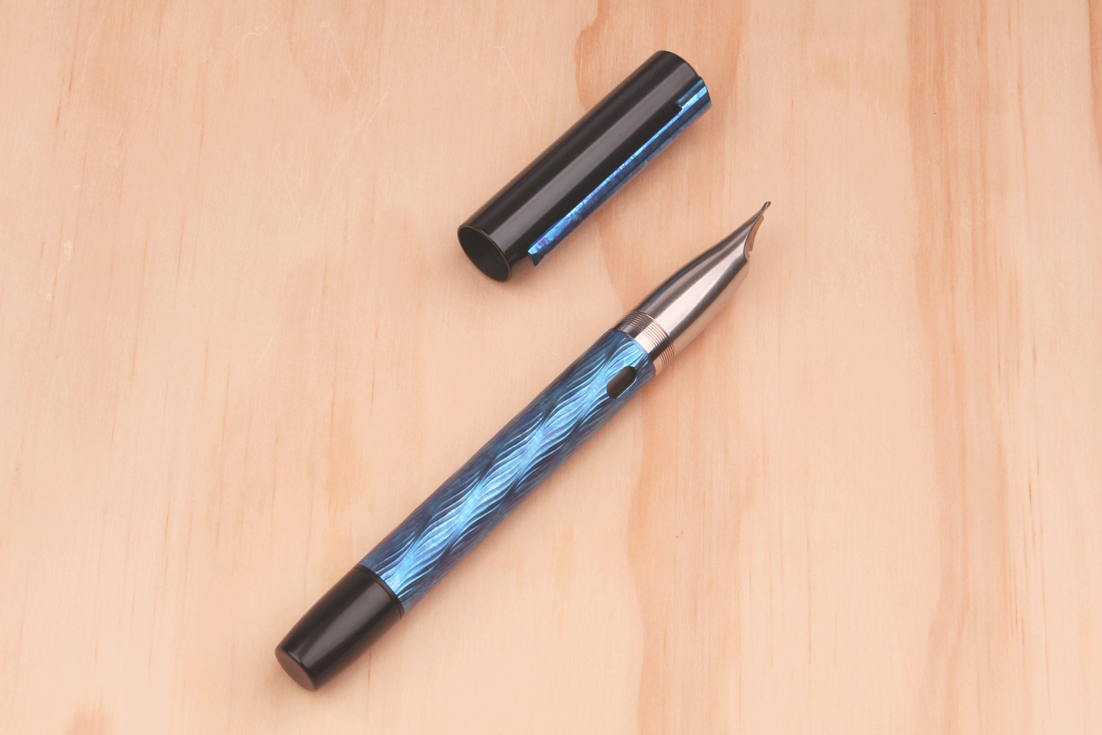 A metal fountain pen with a blue, guilloched body, an integrated nib, and black back and cap. The cap also has a blue guilloched clip. 