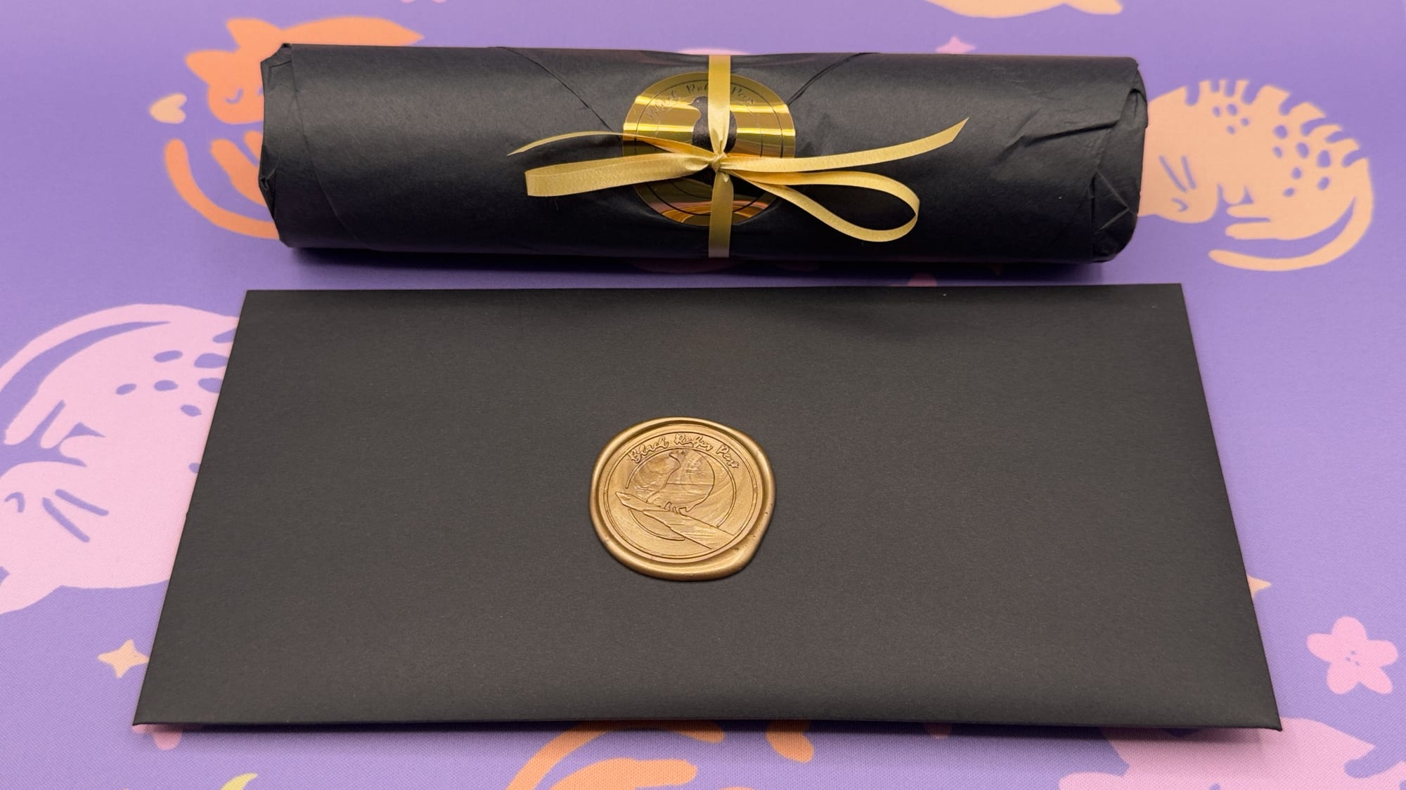 Aforementioned envelope and wrapped cylinder, both in black with gold "trim" -- gold wax seal on the black envelope, and gold ribbon and sticker on the black wrapped cylinder