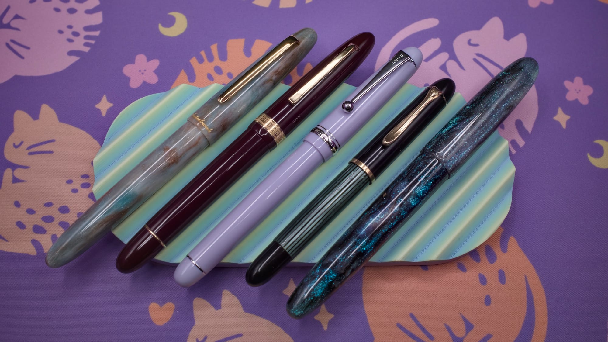 5 cigar-shaped fountain pens of varying sizes and materials sitting on a pastel green and yellow pen tray