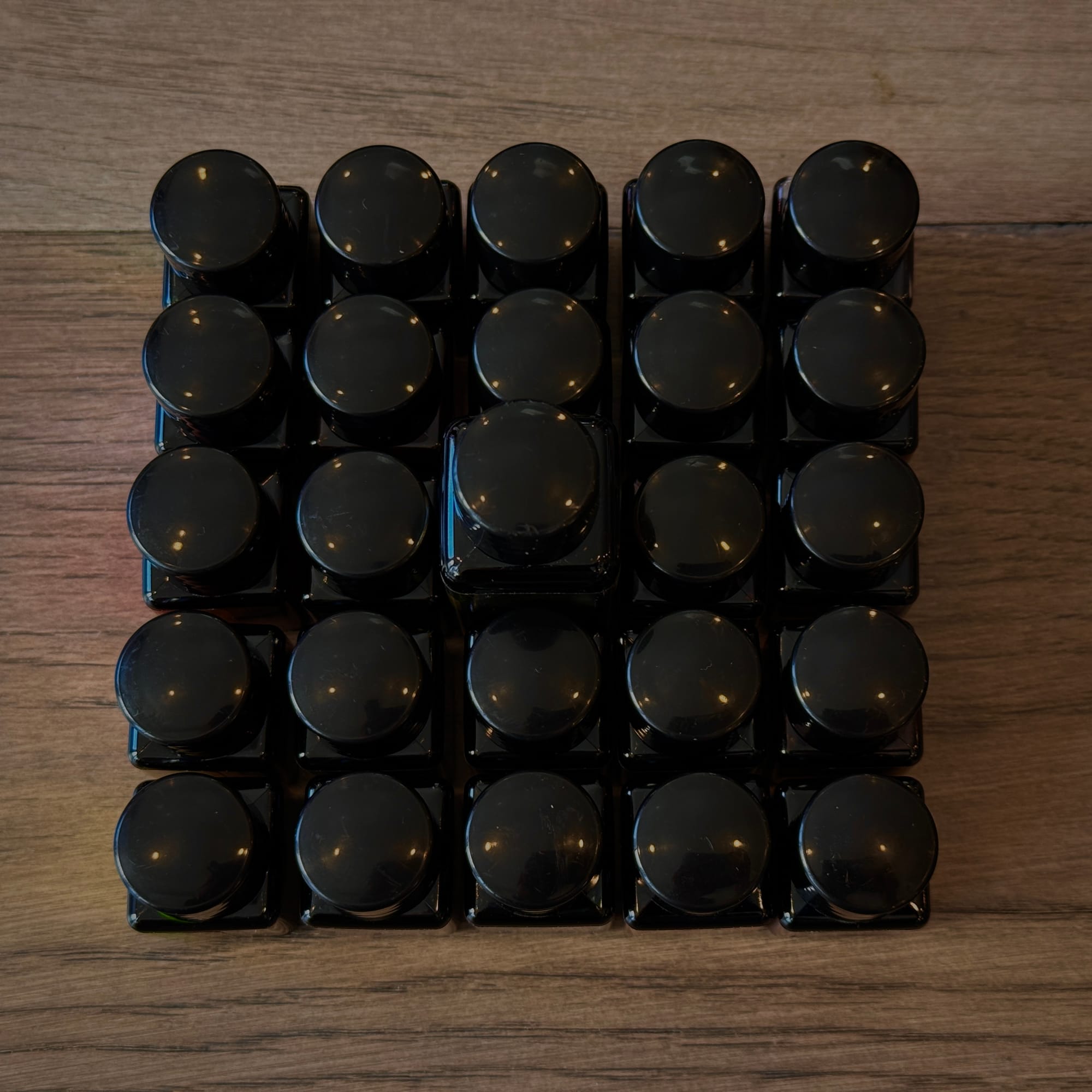 25 square bottles of ink arranged in a grid, with the tallest in the center and the others filling out the rest of the 5x5 grid