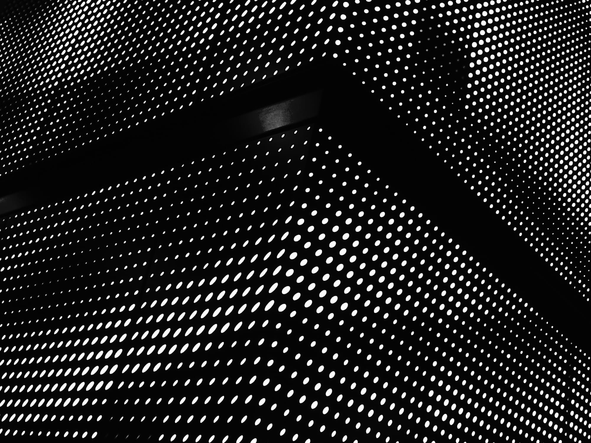 Black and white abstract picture of a grid of white dots, some round, some oblong, with a dark stripe wrapping around a corner, in the middle of the patterned dots