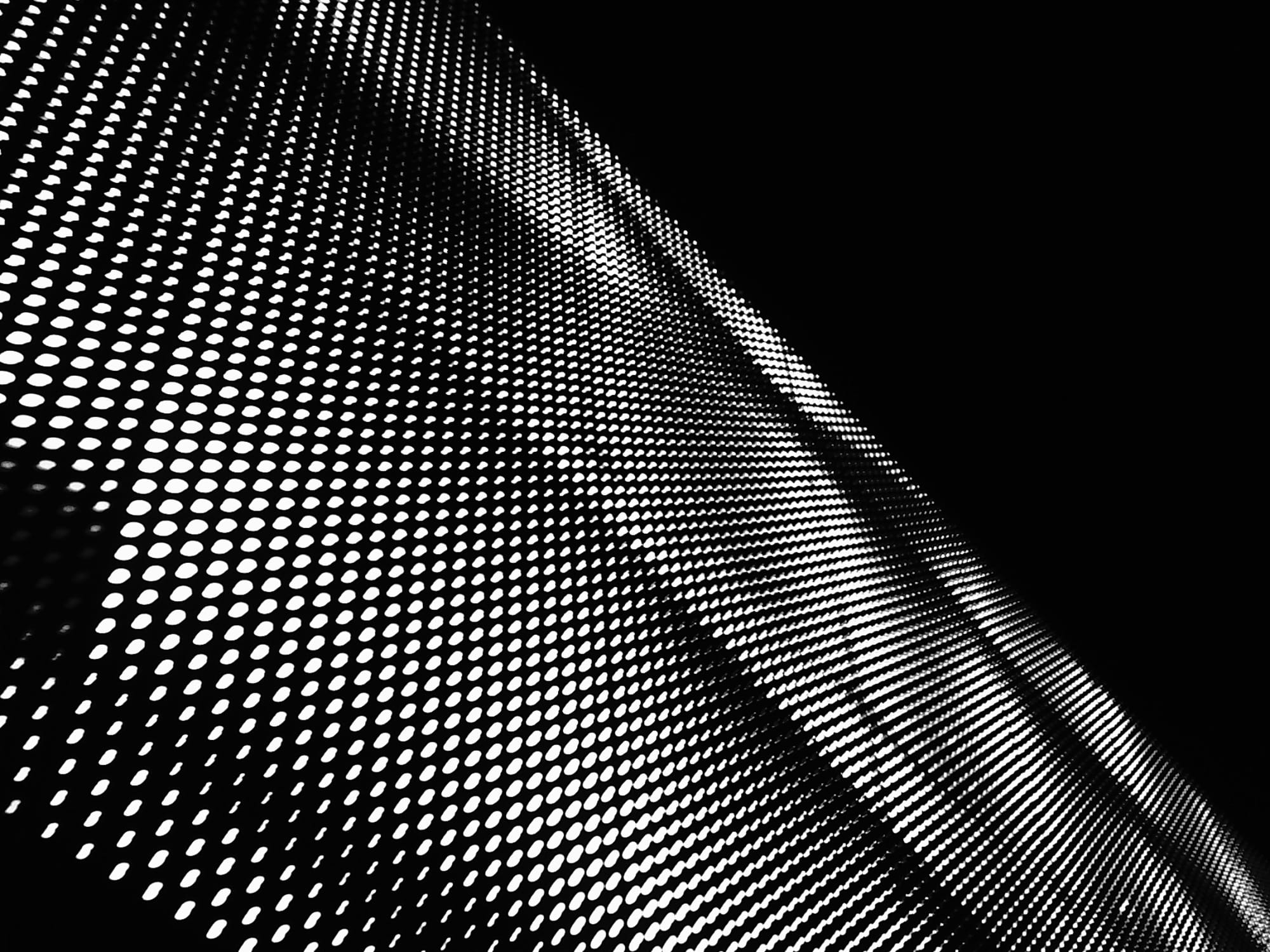 Black and white abstract picture of a grid of white dots on a black surface, with a triangle of black sky taking up the top right corner of the frame