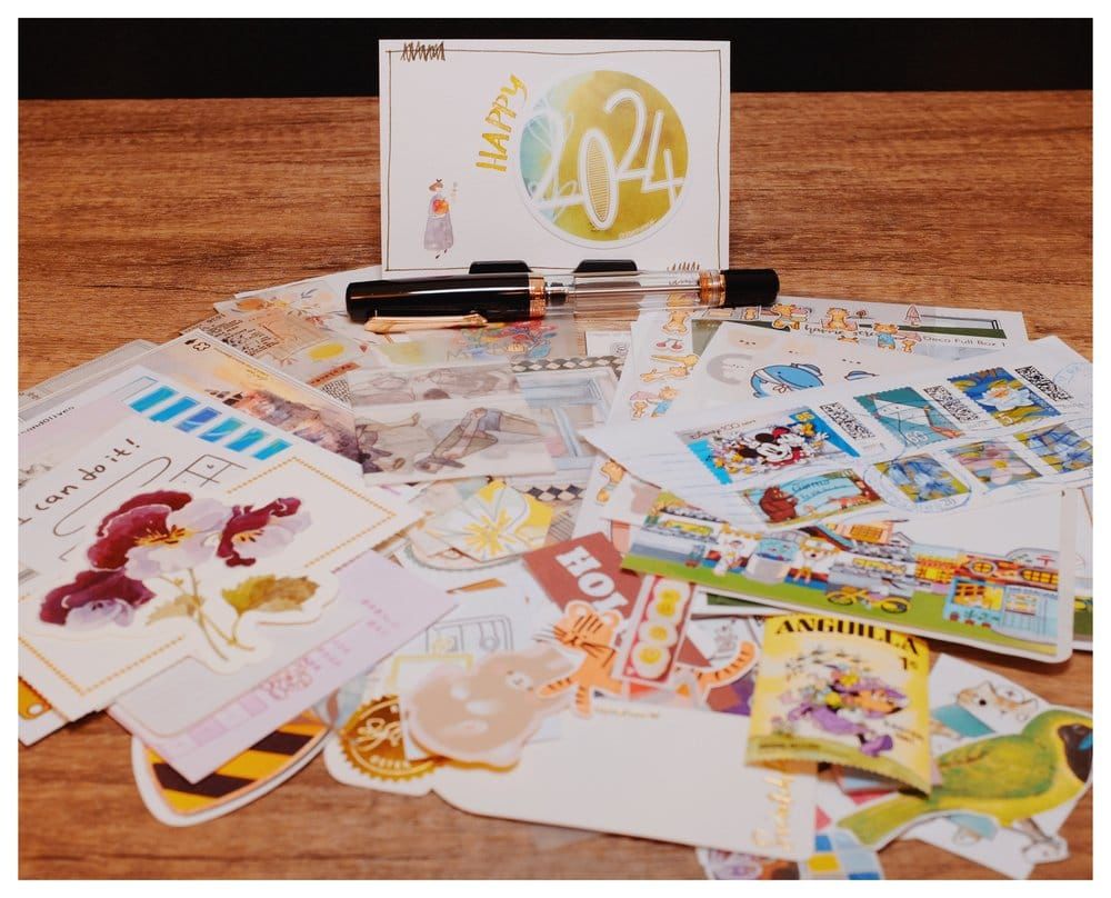 A pile of stationery ephemera laid out in front of a "happy 2024" card and a black and rose gold fountain pen