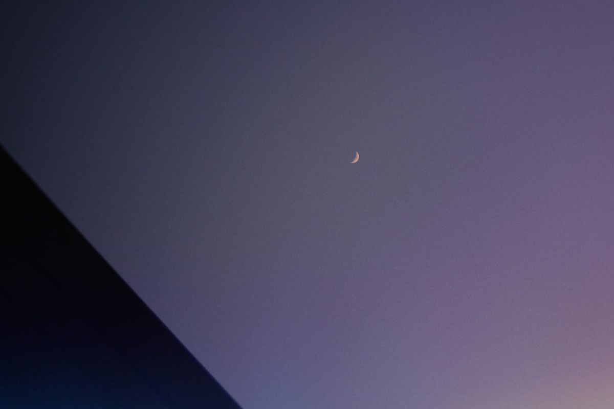 Very small crescent moon near the middle of the frame, with a black triangle in the lower left corner