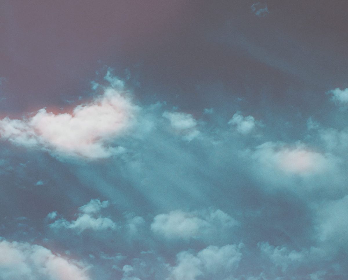 Hazy, dreamy picture of poofy clouds in a dramatic sky with diagonal trails, similar to “god ray” sunlight
