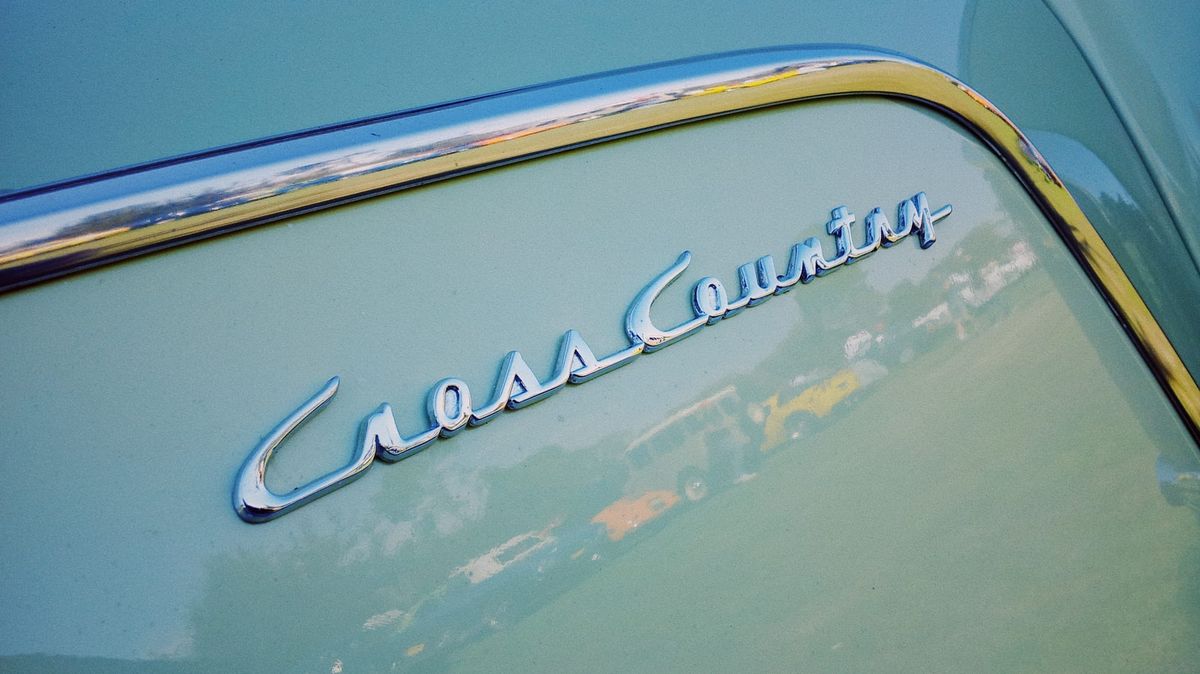Close up of a vintage chrome logo on an old pastel green car that says "CrossCountry" in a kind of script font