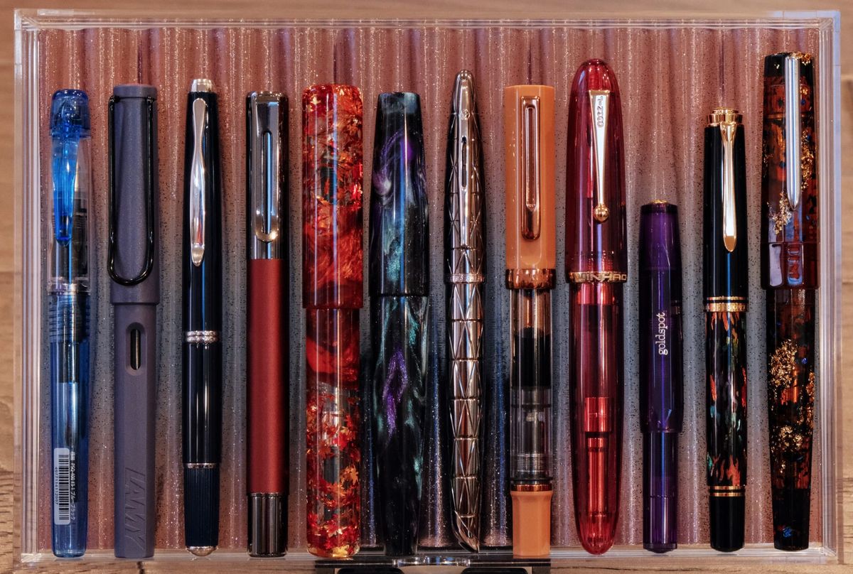 Overhead view of an acrylic drawer with a 3D-printed pen tray containing 12 fountain pens of different shapes and designs