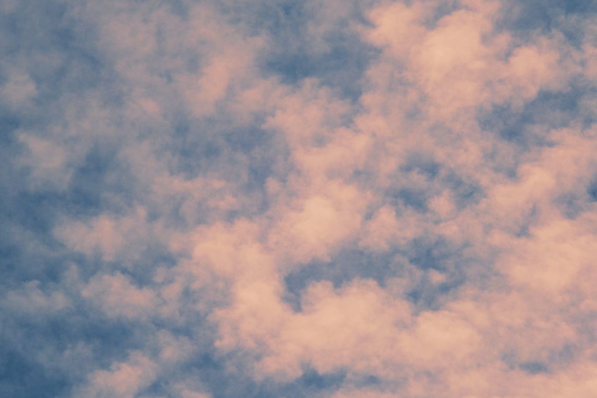 Pink-orange tinged, puffy clouds filling a medium-dark blue sky, some clouds more brightly lit from the middle to the right edge of the frame