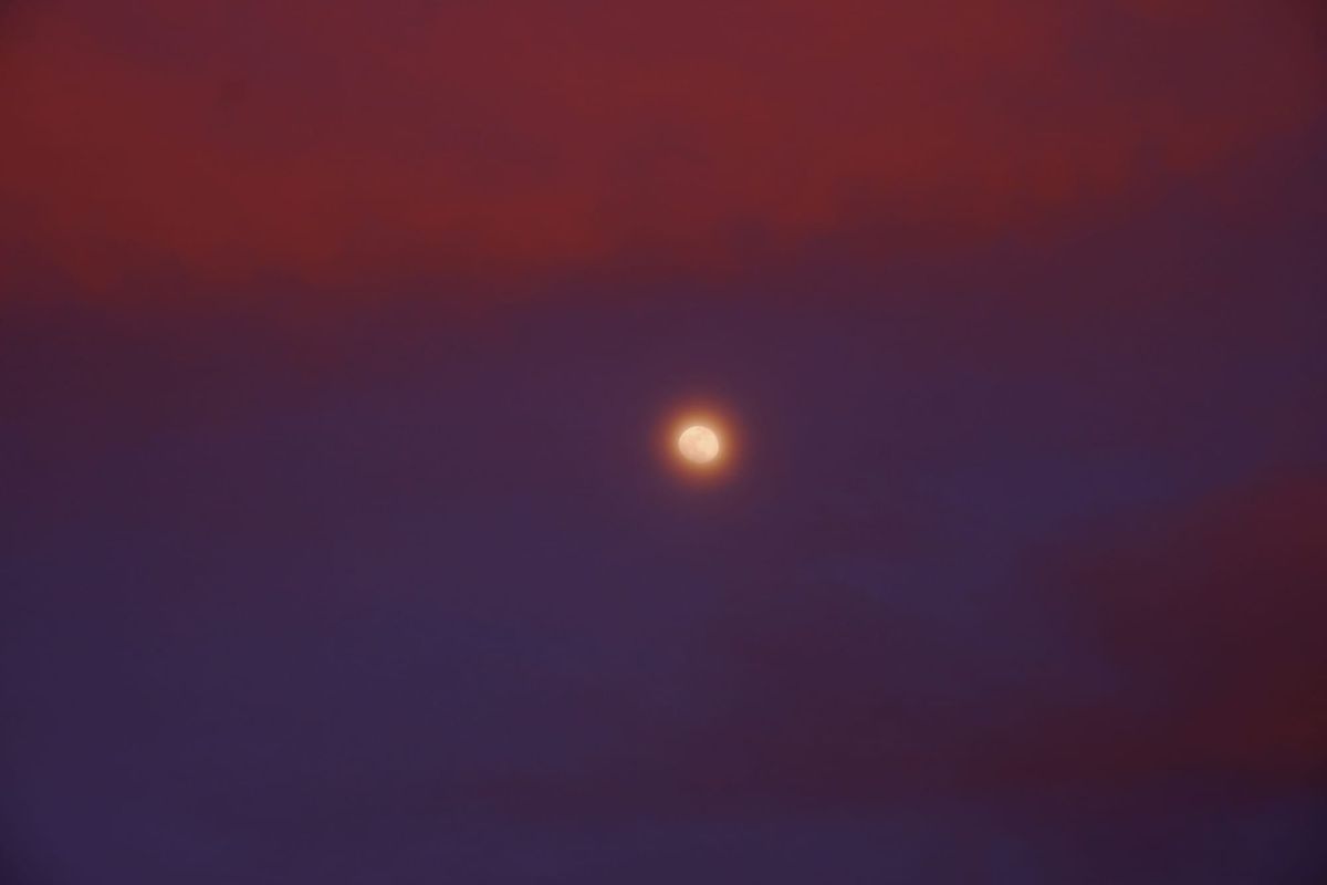 Hazy, haloed moon set in a deep blue-purple sky with vivid red-pink clouds above and below