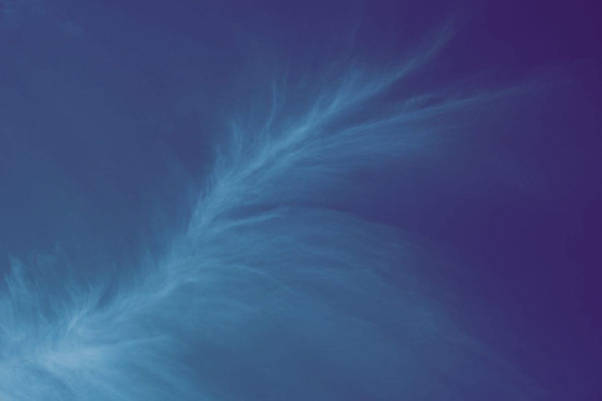 A very wispy cloud "spray" snaking diagonally across the frame from lower left to upper right; faint light blue against a dark blue-black sky