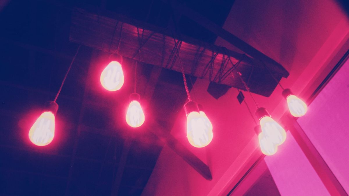 Looking up at bare glass bulbs with visible filaments hanging at different lengths from a wooden bar overhead