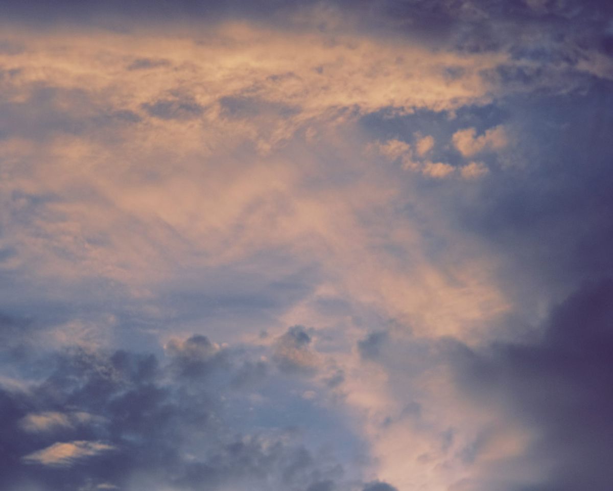 Telephoto image of layers of different clouds in sunset sky with different textures, shapes, and colors from deep blue to peachy white
