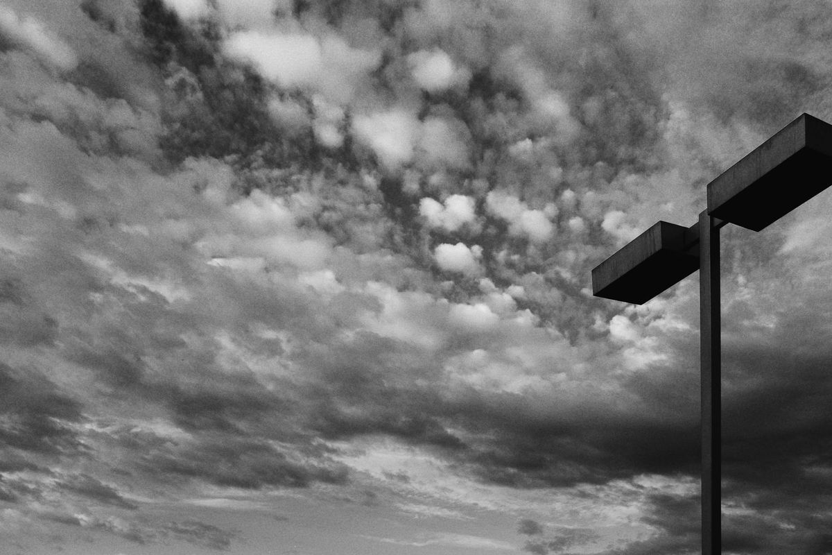 Black and white image of a cloud-blanketed sky and a parking lot light on the right of the frame