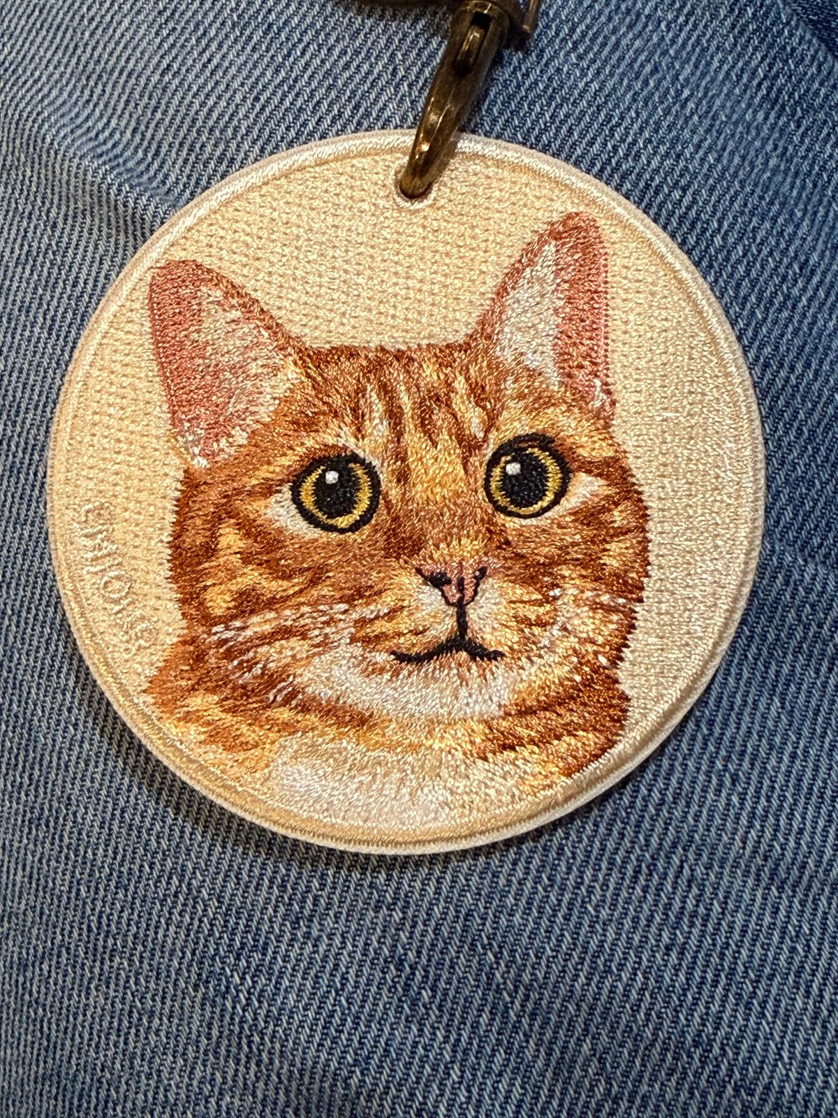 Embroidered patch with a portrait of an orange and cream tabby against a cream-colored background