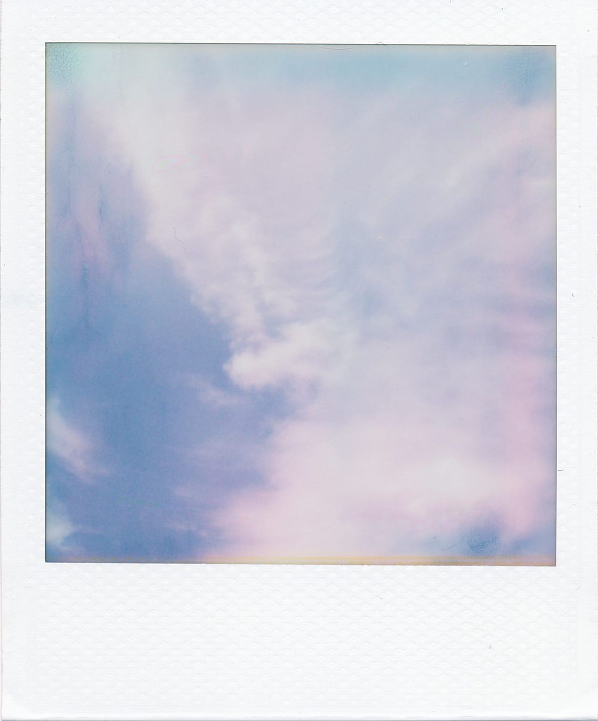 Polaroid Go picture of an organic cloud formation in the blue sky with random film development artifacts around the edge of the frame