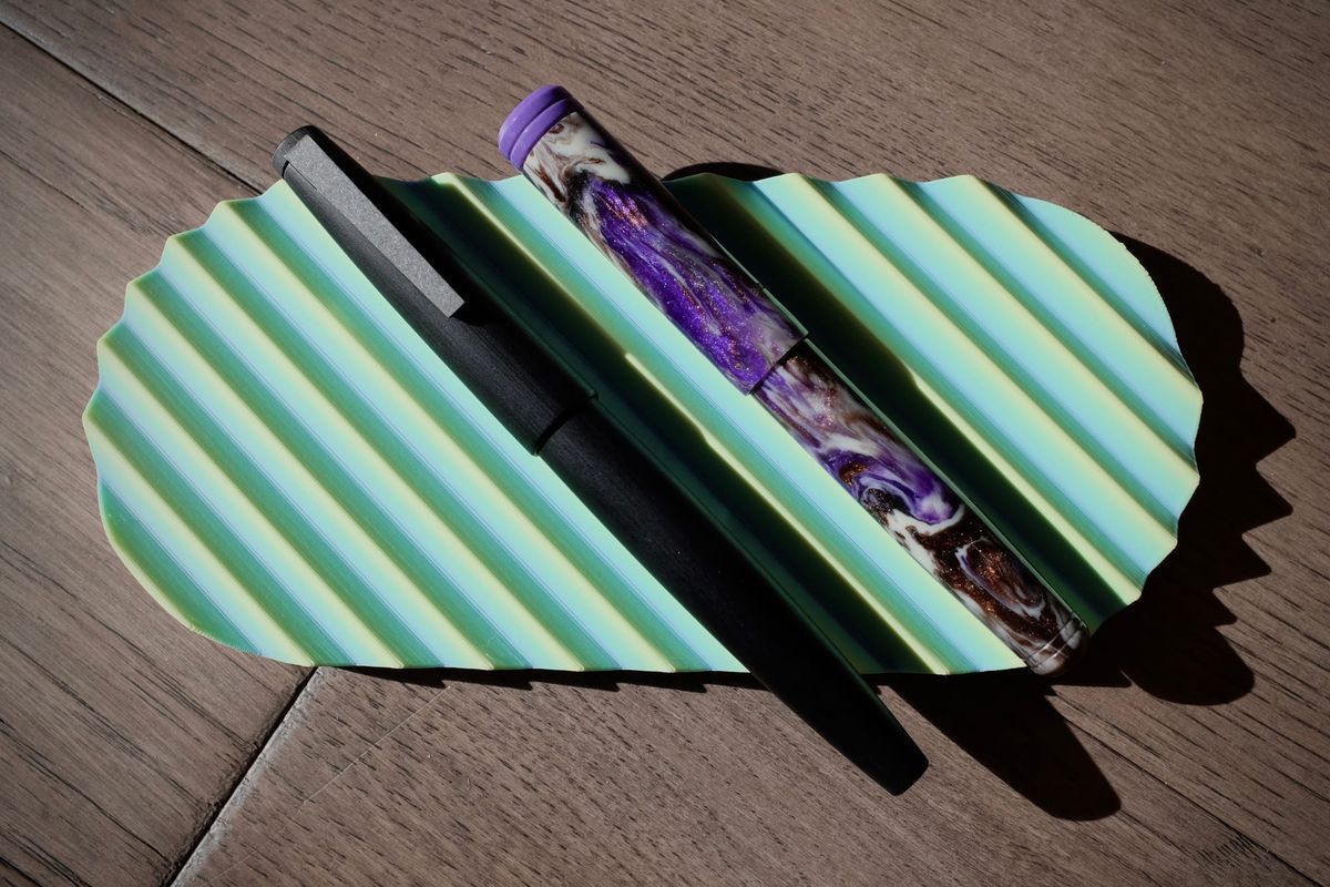 2 fountain pens sitting on a pastel seafoam green pen tray: a black Lamy 2000 (left) and a Franklin-Christoph p20 in purple, brown, and cream swirl resin (right)