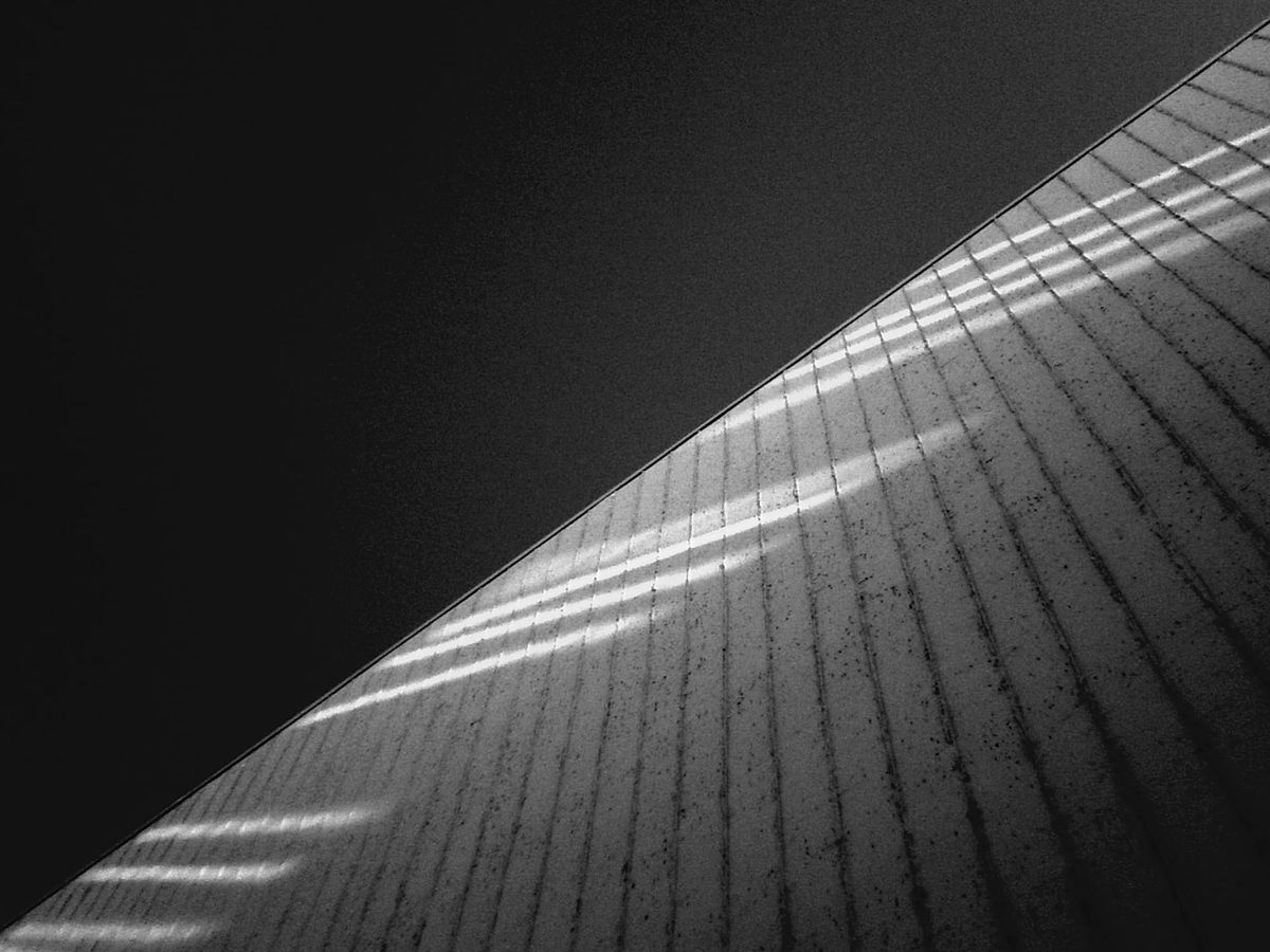 Abstract image of the side of a building with stripes of sunlight, framed diagonally, with darkened sky occupying the rest of the frame