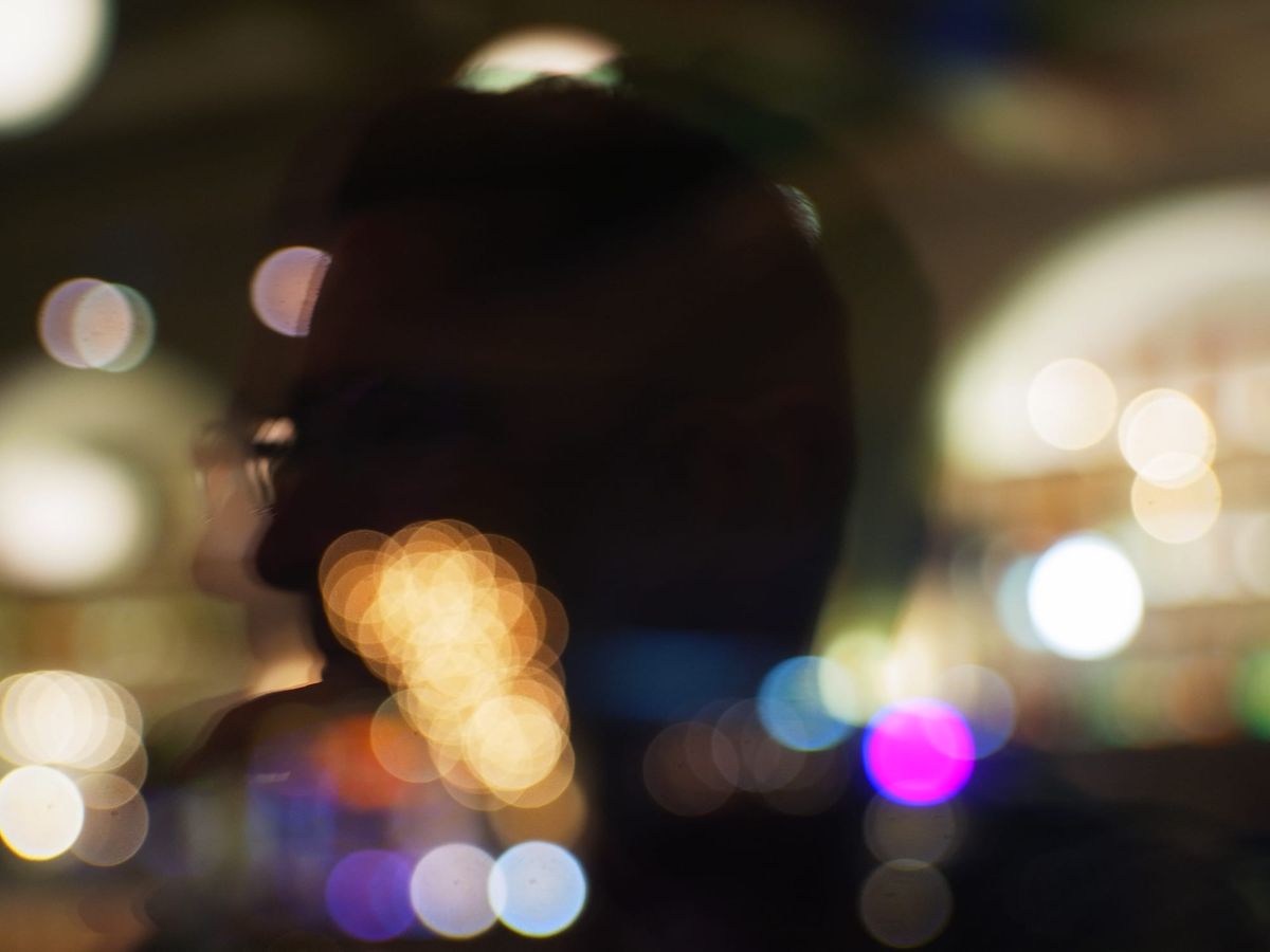 Abstract, dreamy, out of focus picture of someone's profile reflected in a window with many "bokeh balls" randomly sprinkled across the frame
