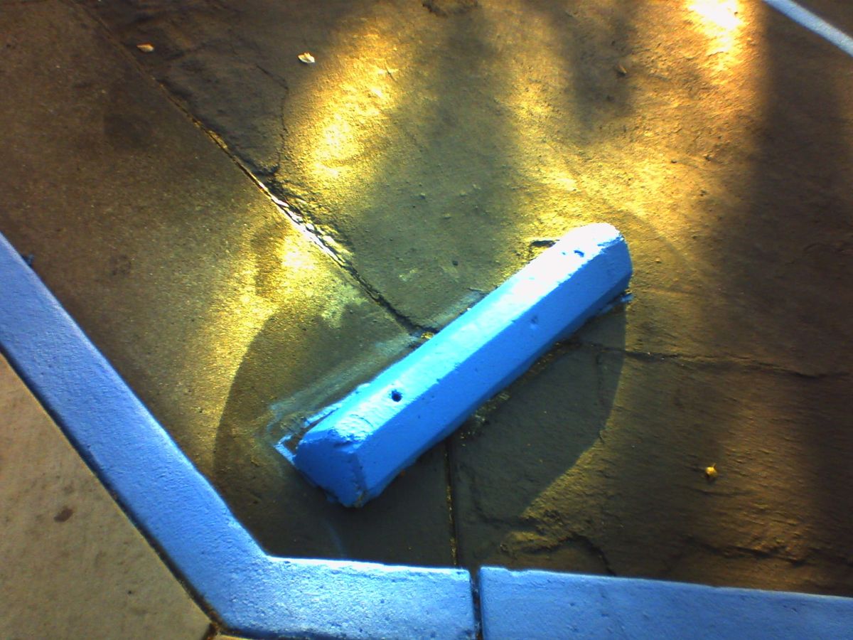 Abstract, low-res picture of a blue parking lot stop and matching painted curb with some bursts of sunlight shining on black pavement