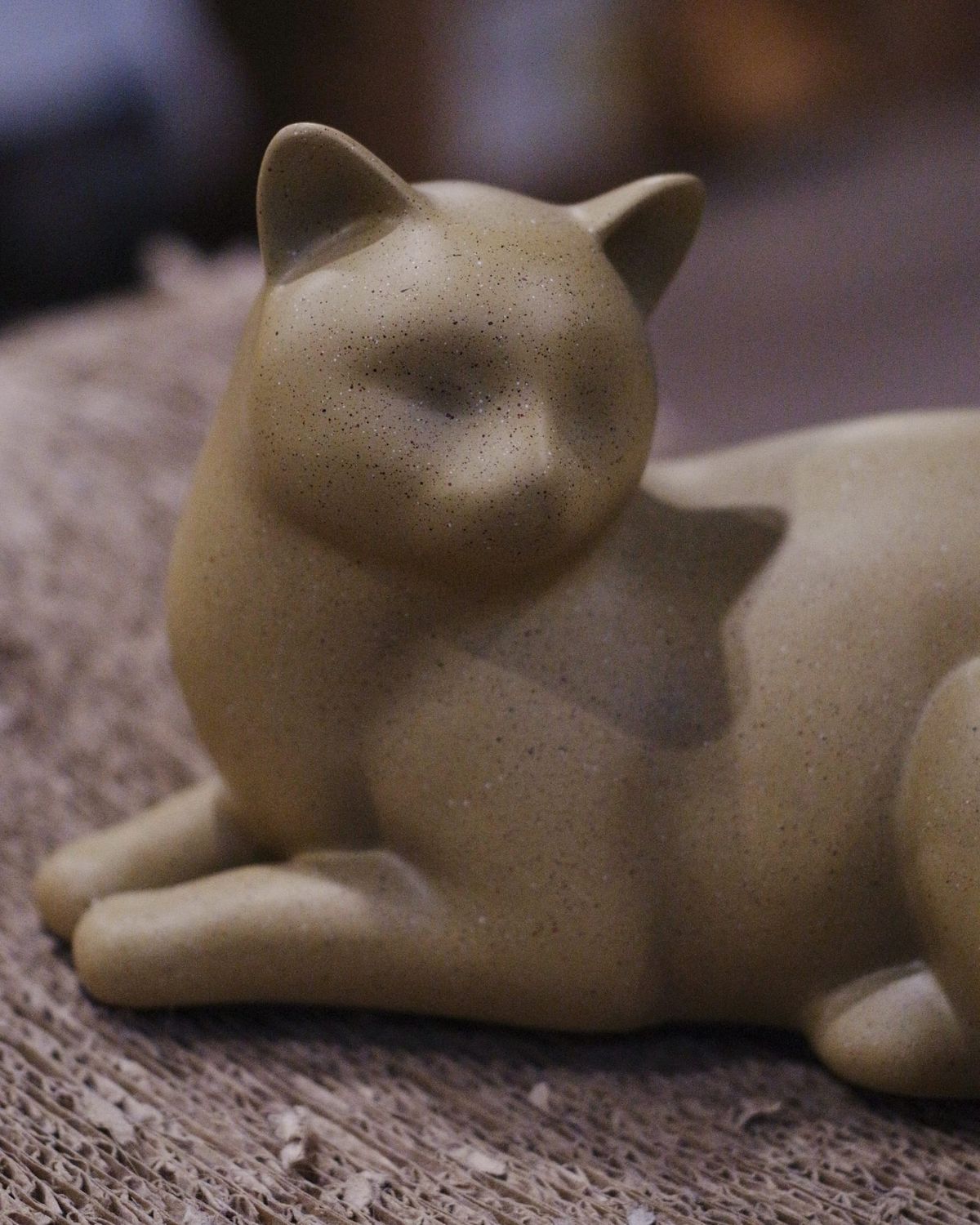 Close up of a tan cat figurine sitting on a cardboard scratcher