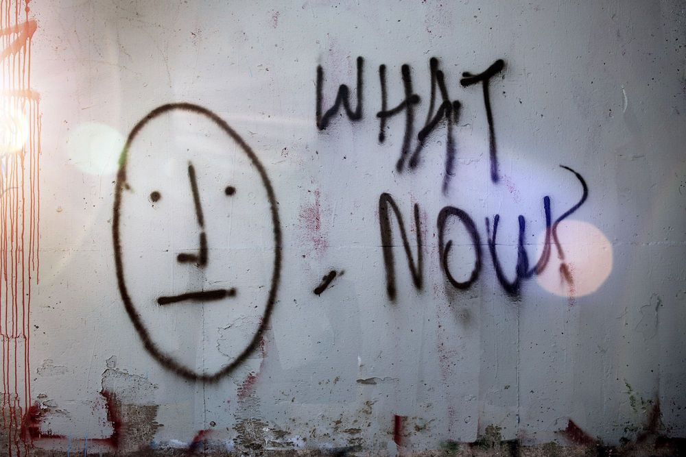 Graffiti of simple face, saying "what now?"