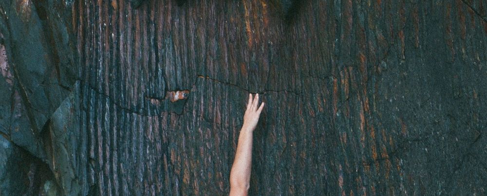 A hand reaching up against a scarred and blackened vertical surface