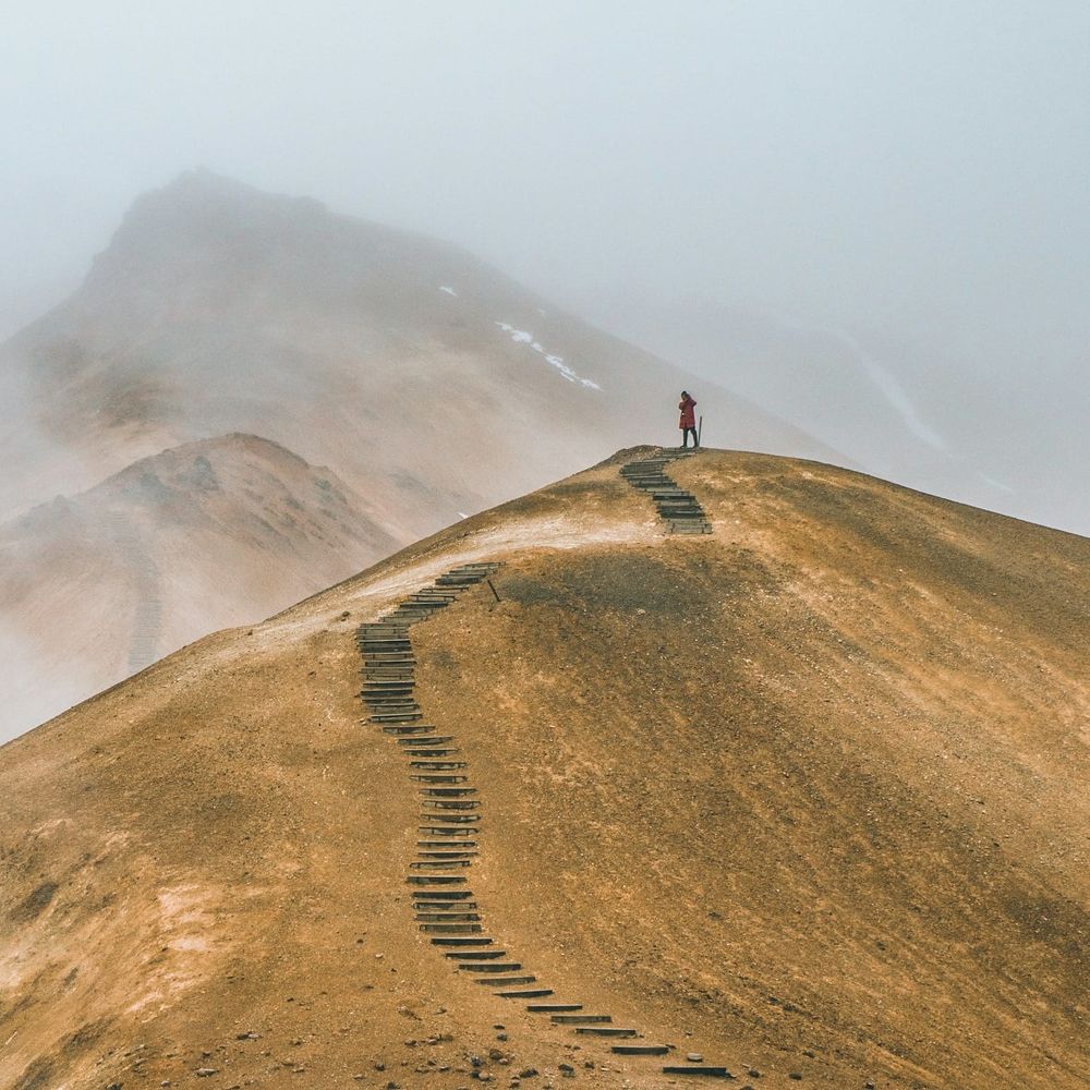 Steps leading up a bare hilltop, with a figure at the top. Peaks are visible in the distance (and more steps)