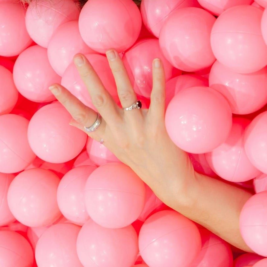 A hand in a ballpit filled with bright pink balls