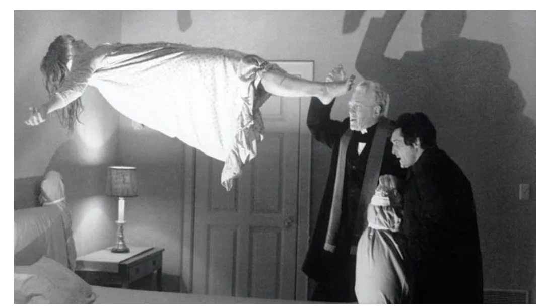 image from the movie The Exorcist. girl levitating above a bed while a priest etc works on her