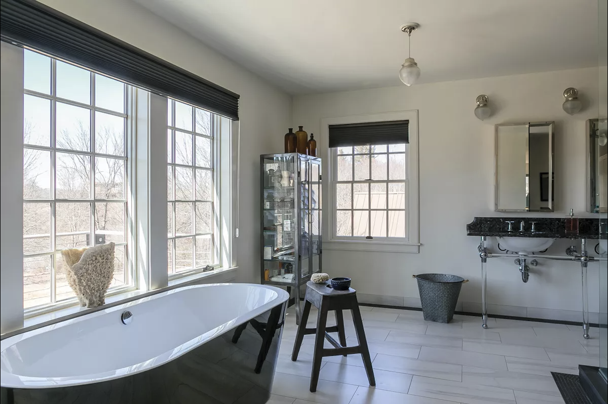 The primary bathroom is an extension of the bedroom and maximizes the lake view. “The whole second floor was about creating private spaces,” says Stabilito. “I wanted it to feel separate from the rest of the house, like its own retreat.” For the floor, Stabilito used white porcelain tile to resemble marble and accented it a black mosaic tile border. The freestanding tub faces the lake. Stabilito added Duravit and Toto fixtures throughout the space. - Winona Barton-Ballentine The primary bathroom is an extension of the bedroom and maximizes the lake view. “The whole second floor was about creating private spaces,” says Stabilito. “I wanted it to feel separate from the rest of the house, like its own retreat.” For the floor, Stabilito used white porcelain tile to resemble marble and accented it a black mosaic tile border. The freestanding tub faces the lake. Stabilito added Duravit and Toto fixtures throughout the space. - Winona Barton-Ballentine