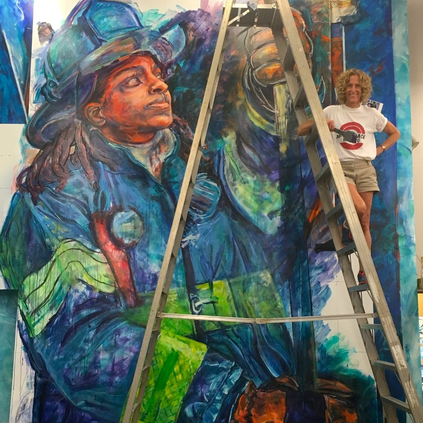 AMP Founder and Artistic Director&nbsp;Ellen Griesediek perches on a ladder at right.