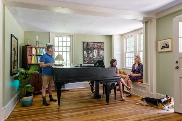 The Reisfelds in the home&rsquo;s original living room. The grand piano came from a church in Lakeville. Hanging on the far wall is a painting of the Little Deep in Woodstock by Kathy Reisfeld&rsquo;s mother, Sharon Stanfield. The family corgi, Taco, looks out a backdoor.