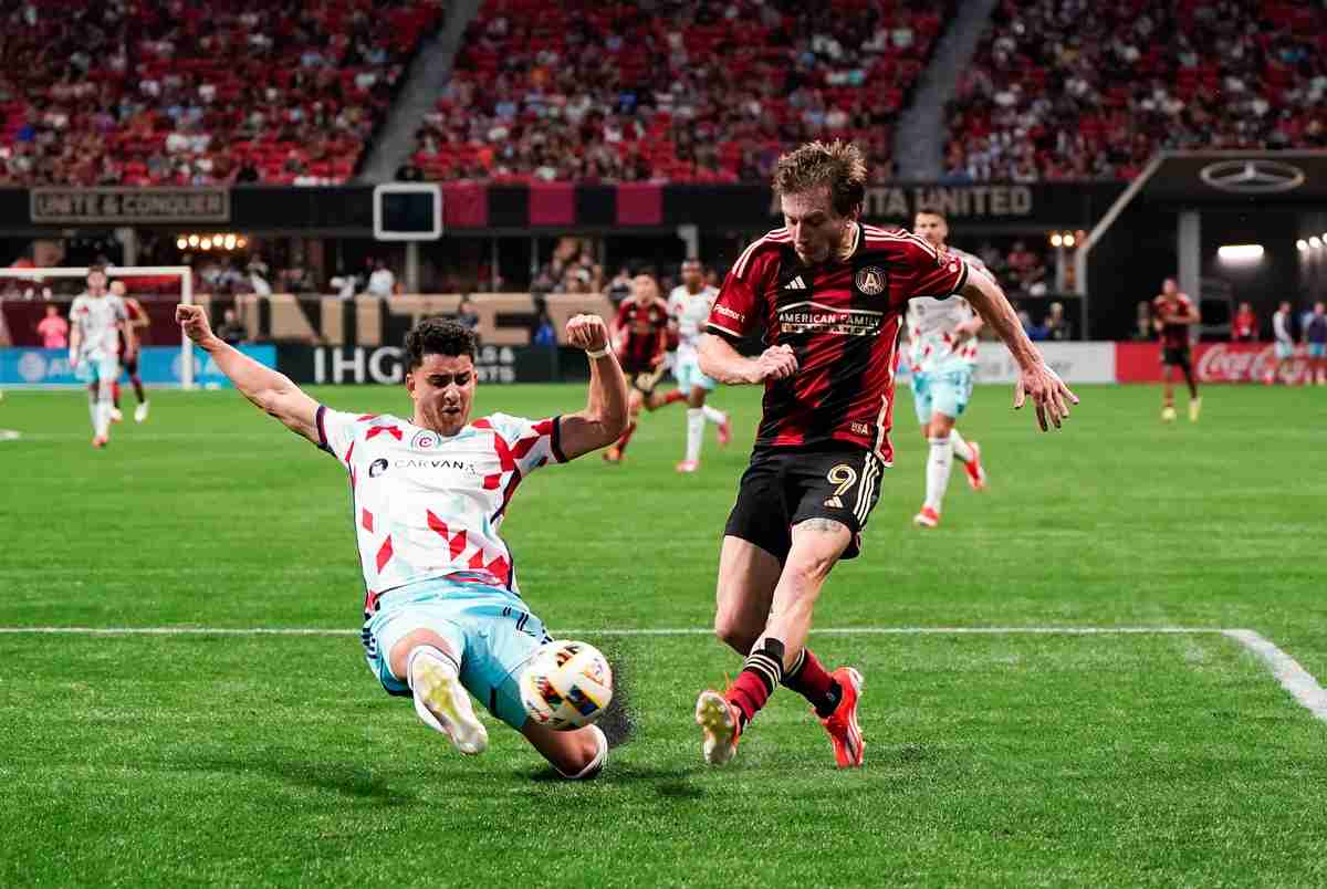 Two soccer players play for the ball during a soccer game. One is sliding to try to make a tackle, the other is trying to play the ball past him. 