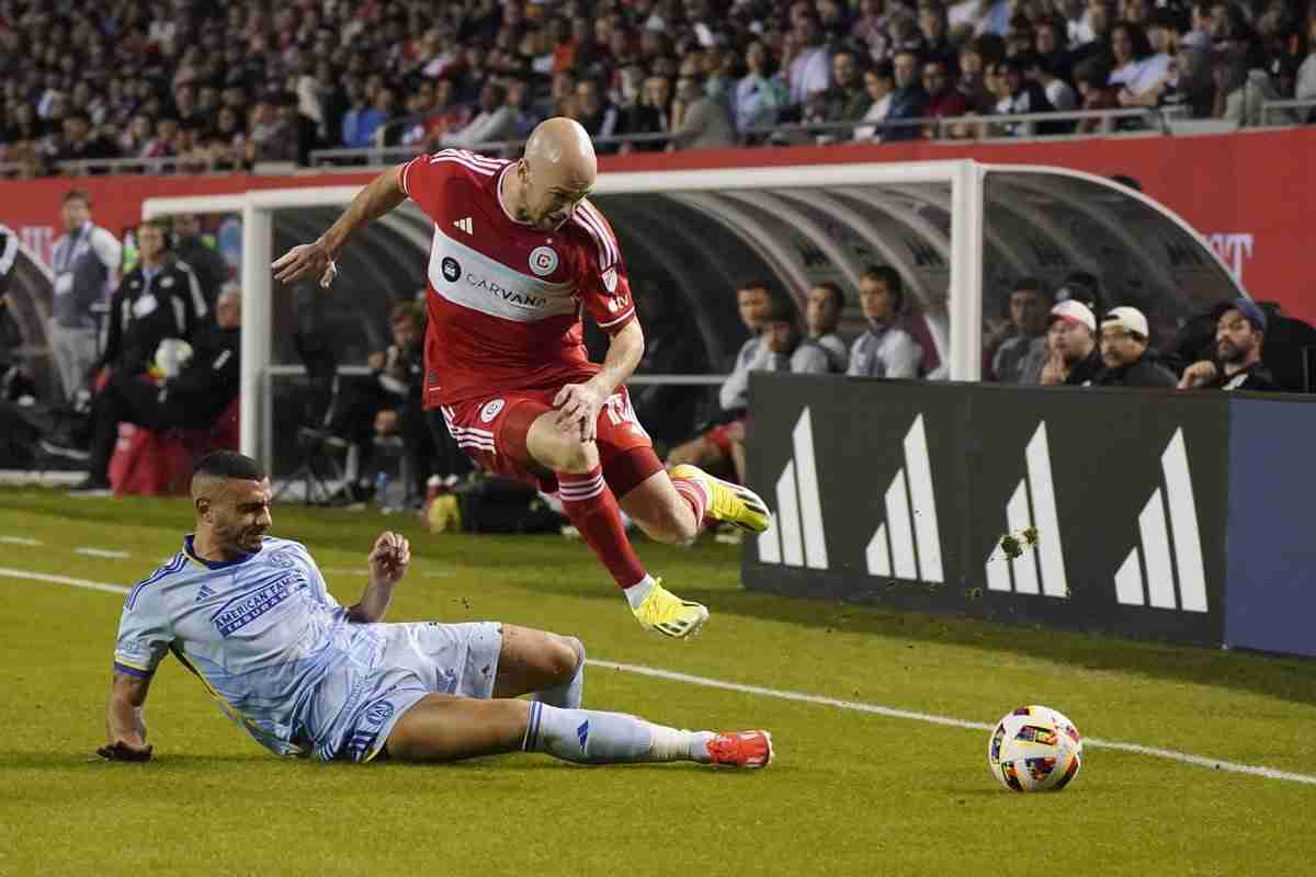 A soccer playerj umps over another during a game.