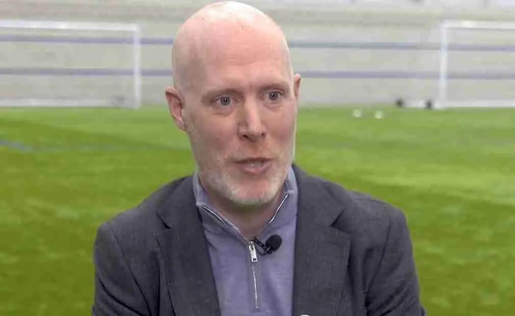Close in shot of Gregg Blackburn, wearing a jacket and blue shirt on a training pitch.
