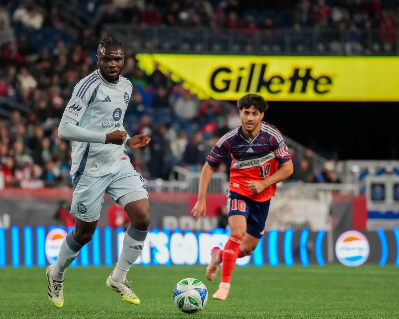 Rominigue Kouamé plays the ball forward against Carles Gil during the Chicago Fire's game against the New England Revolution