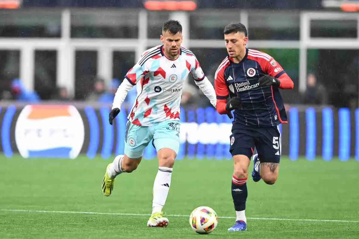 Two soccer players go for the ball during a rainy soccer game