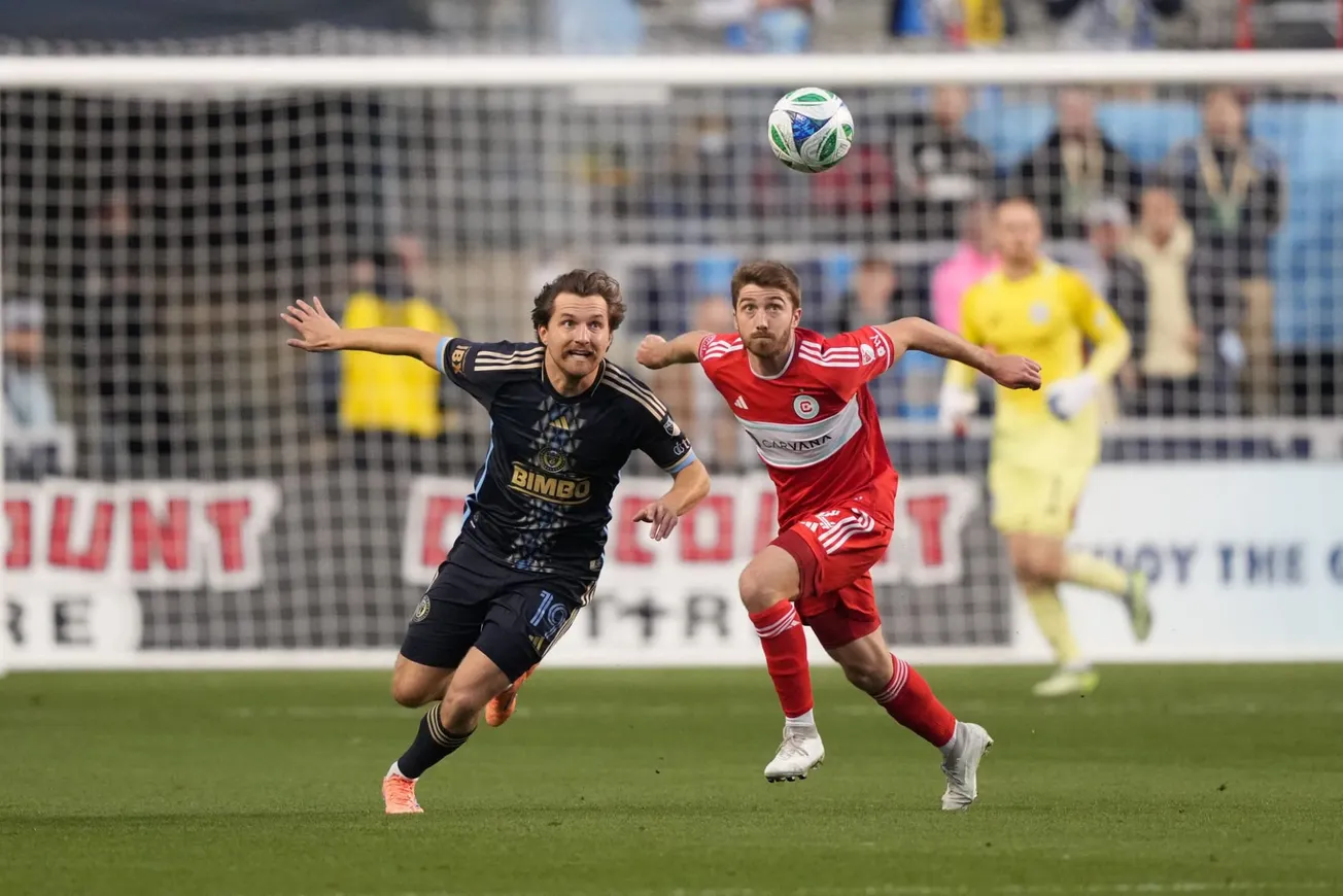 Jonathan Dean (red, on right) and Indiana Vassilev (#19, blue, left) playing soccer 10/26/25