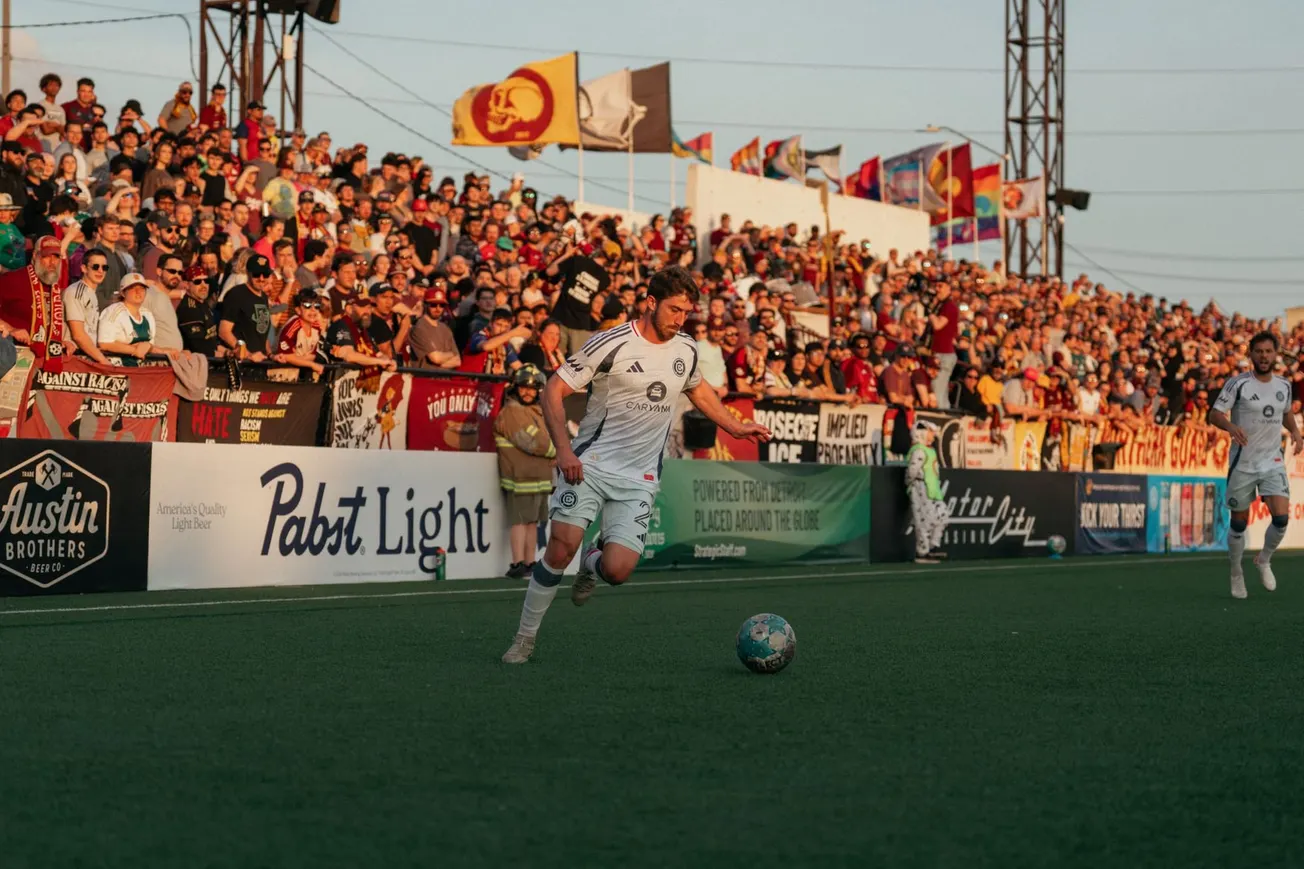 Jonathan Dean plays soccer with the Detroit City crowd in the background near sunset