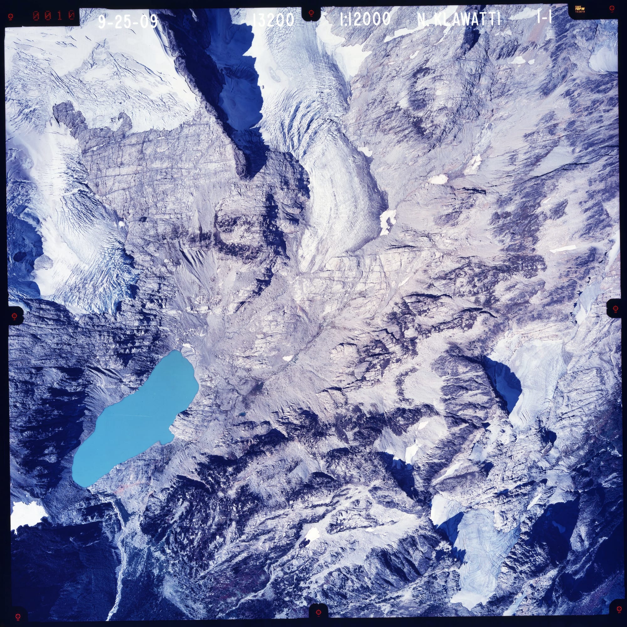 Color aerial photograph of glacier, snowfields and alpine lake on mountain peak.