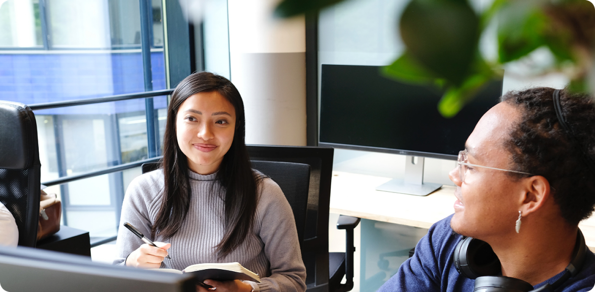 Two coworkers in conversation at modern desk setup, illustrating the need for support in successful AI deployment